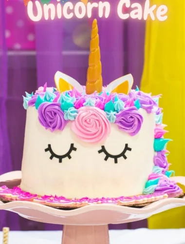 A beautifully decorated unicorn cake with pastel-colored frosting, a golden horn, and a mane of swirled buttercream rosettes in pink, purple, and blue.