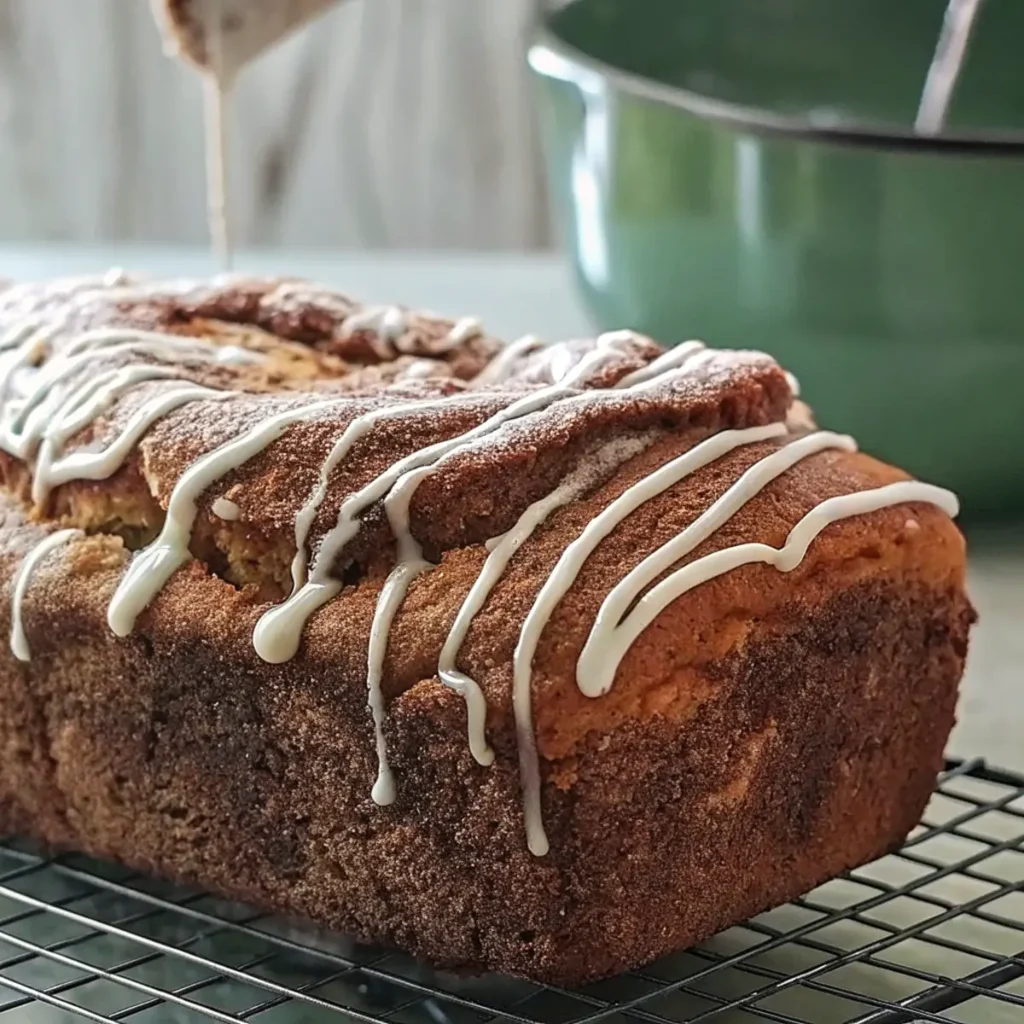 a Gluten Free Cinnamon Swirl Bread with white icing on a cooling rack